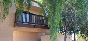 Second-floor balcony with dark wooden railings and lush greenery.